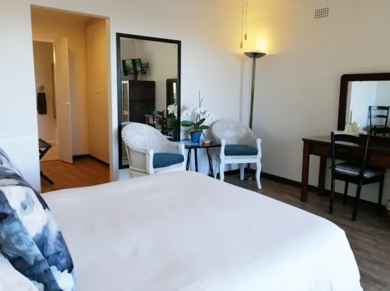 Bedroom with white bed two chairs mirror and desk with lamp