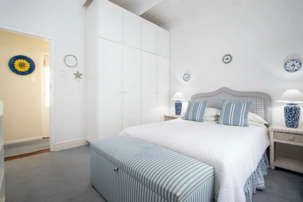White bedroom with blue accents large bed and striped bench at foot