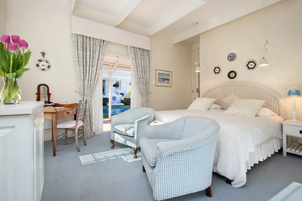 Cozy bedroom with white bed blue armchairs and French doors to garden