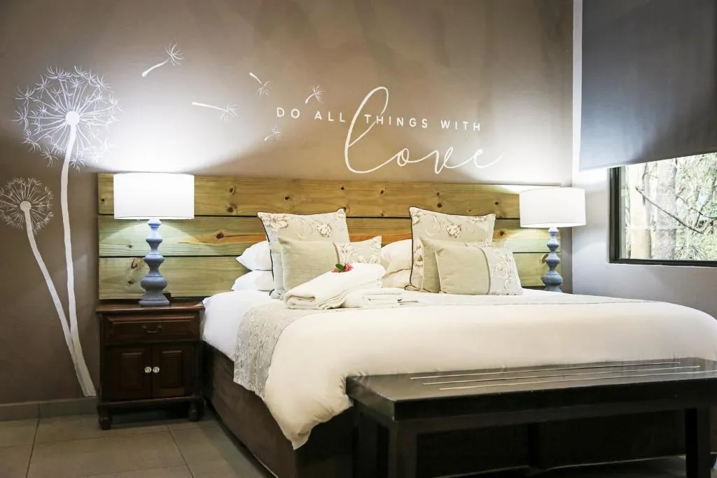 Bedroom with large bed decorative pillows and wall art saying Do all things with love