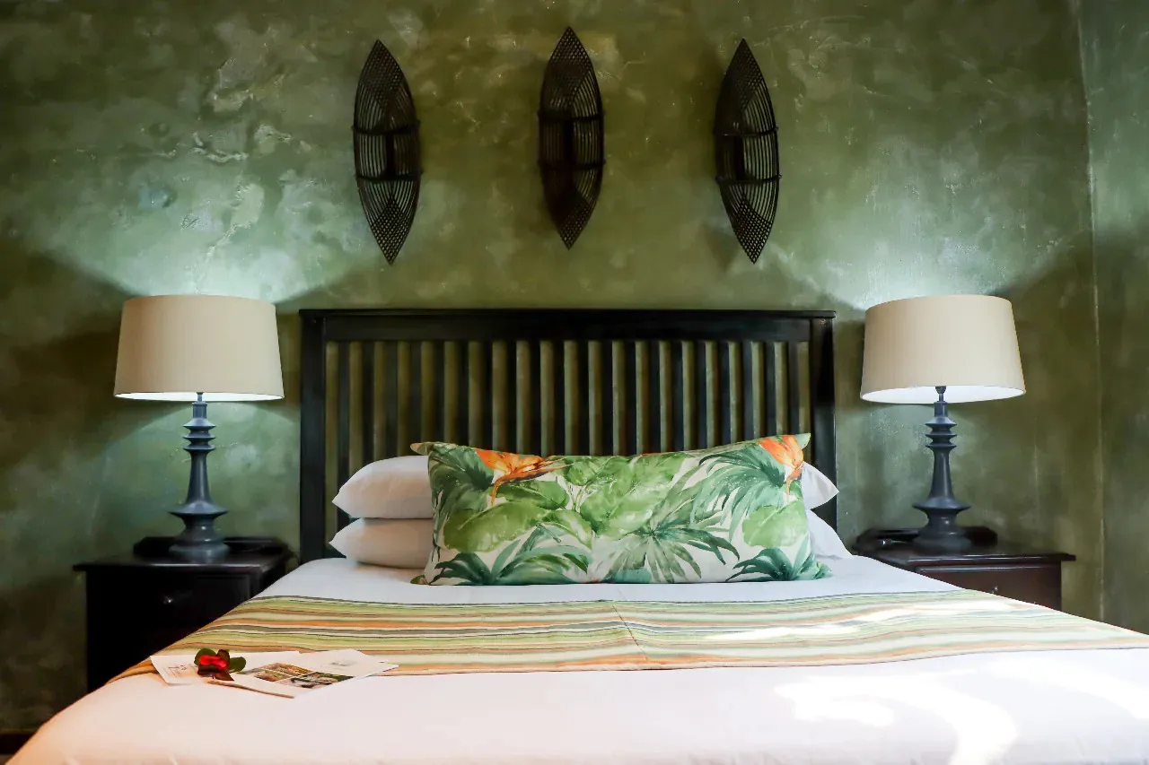 A bed with green tropical pillows flanked by two lamps on nightstands