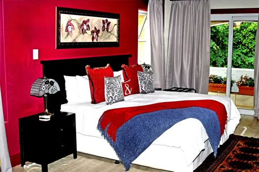 Bedroom with red walls large bed and floral artwork above the headboard