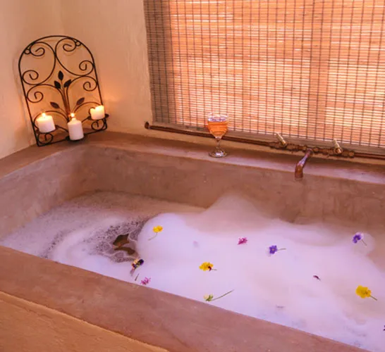 A bathtub filled with bubbles and flowers with candles and a wine glass nearby
