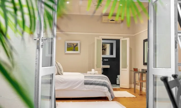 Bedroom with white bed open glass doors and tropical plants outside