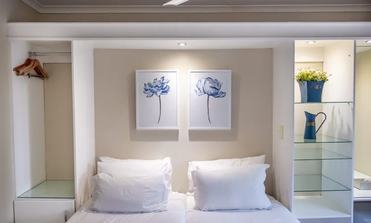 White bed with blue floral artwork above flanked by builtin shelves with decor