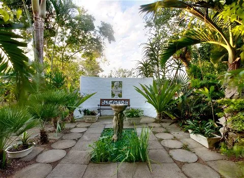 Garden with stone path birdbath bench and lush greenery surrounding a white wall
