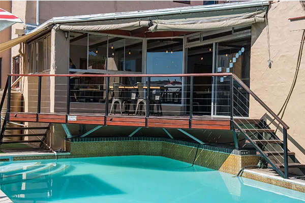 Wooden deck with chairs overlooking a swimming pool and a building