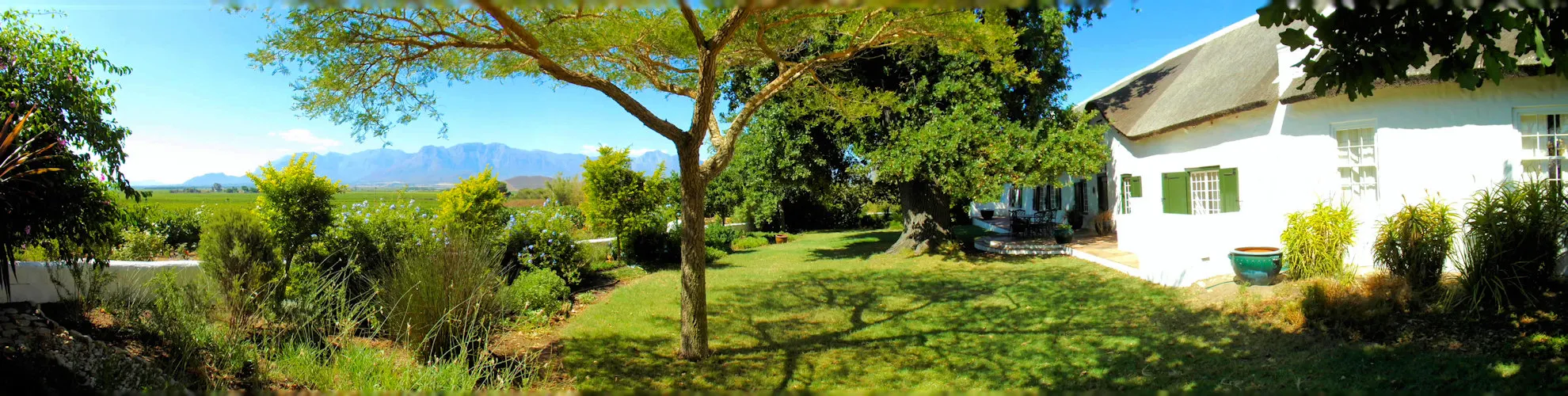 White house with garden trees and distant mountains under a clear blue sky