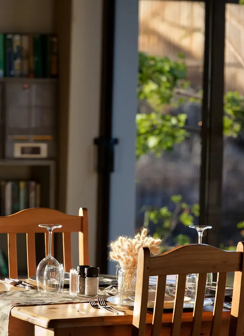 Wooden dining table with glasses cutlery and dried flowers near a window