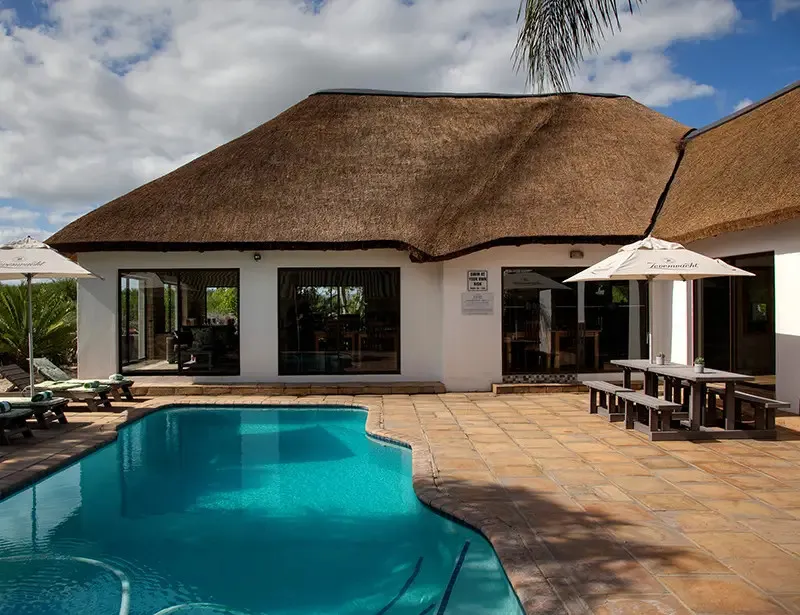 Thatchedroof building with pool lounge chairs and picnic tables under umbrellas