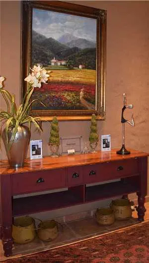 Painting of a countryside scene above a wooden console with decor items
