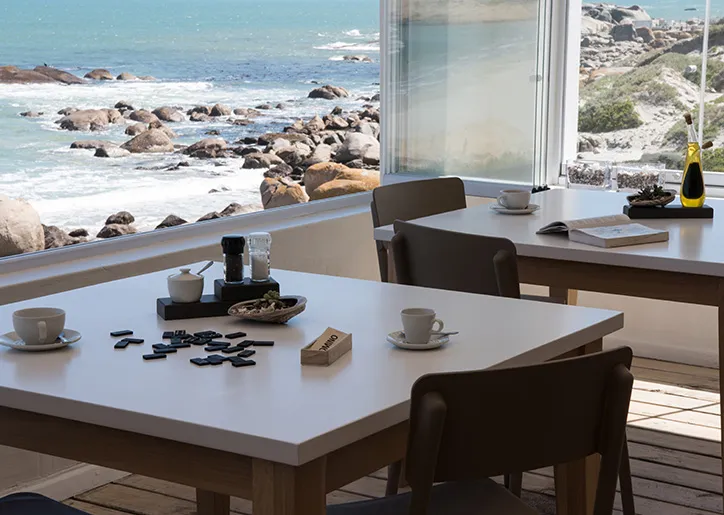 Two tables with coffee cups and dominoes overlooking a rocky ocean shore