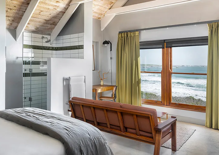 Wooden sofa in bedroom with ocean view through large windows and green curtains