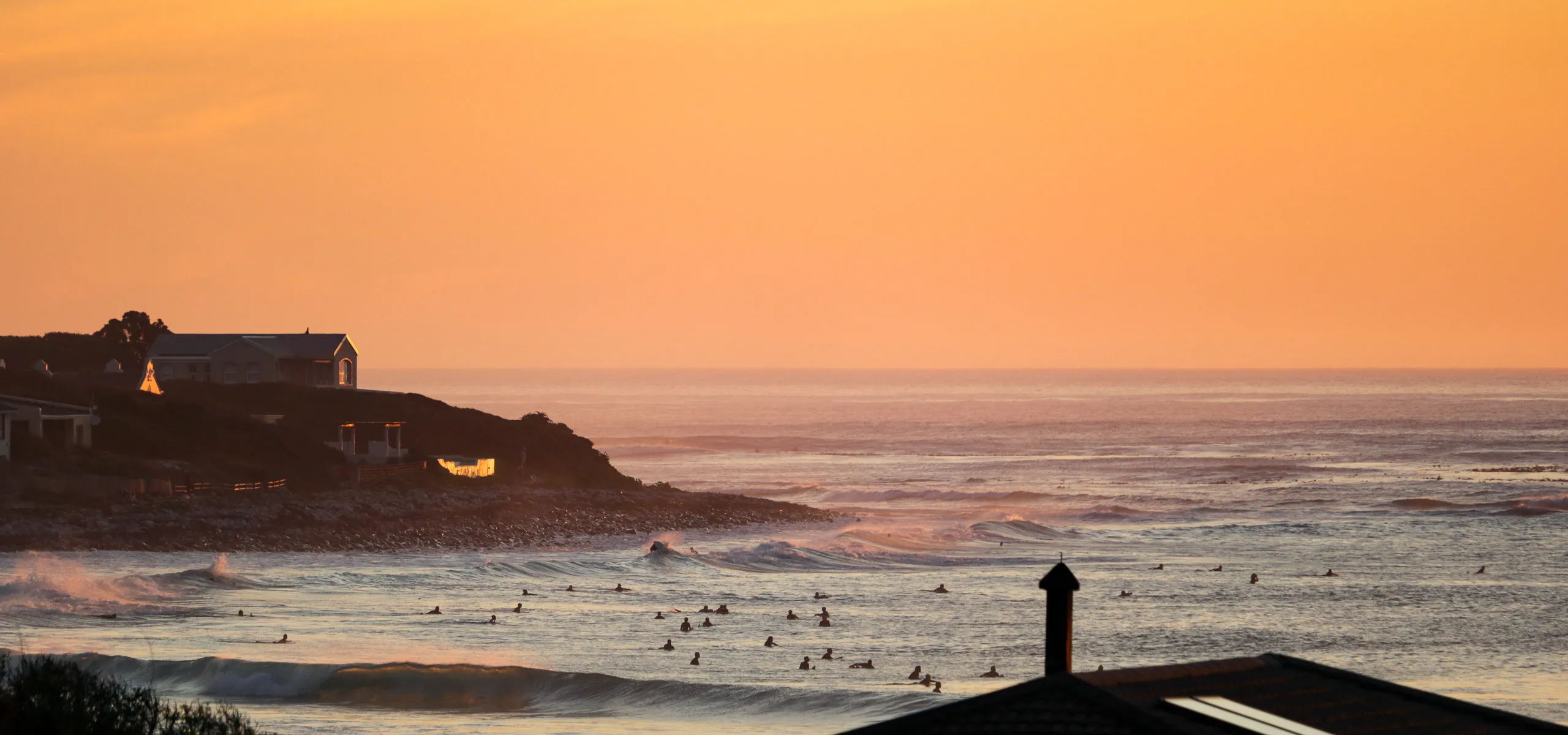 Sunset over ocean with surfers and houses on the shore