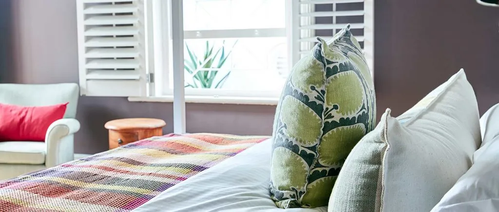 Cozy bedroom with a bed colorful blanket pillows and a window with shutters