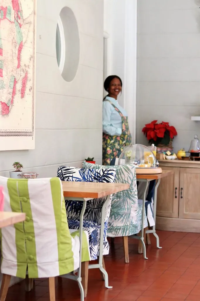 Woman in apron standing in a decorated kitchen with patterned chairs and tables