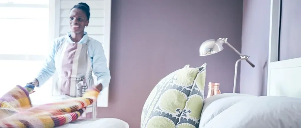 Woman folding blanket in a bedroom with a lamp and pillows