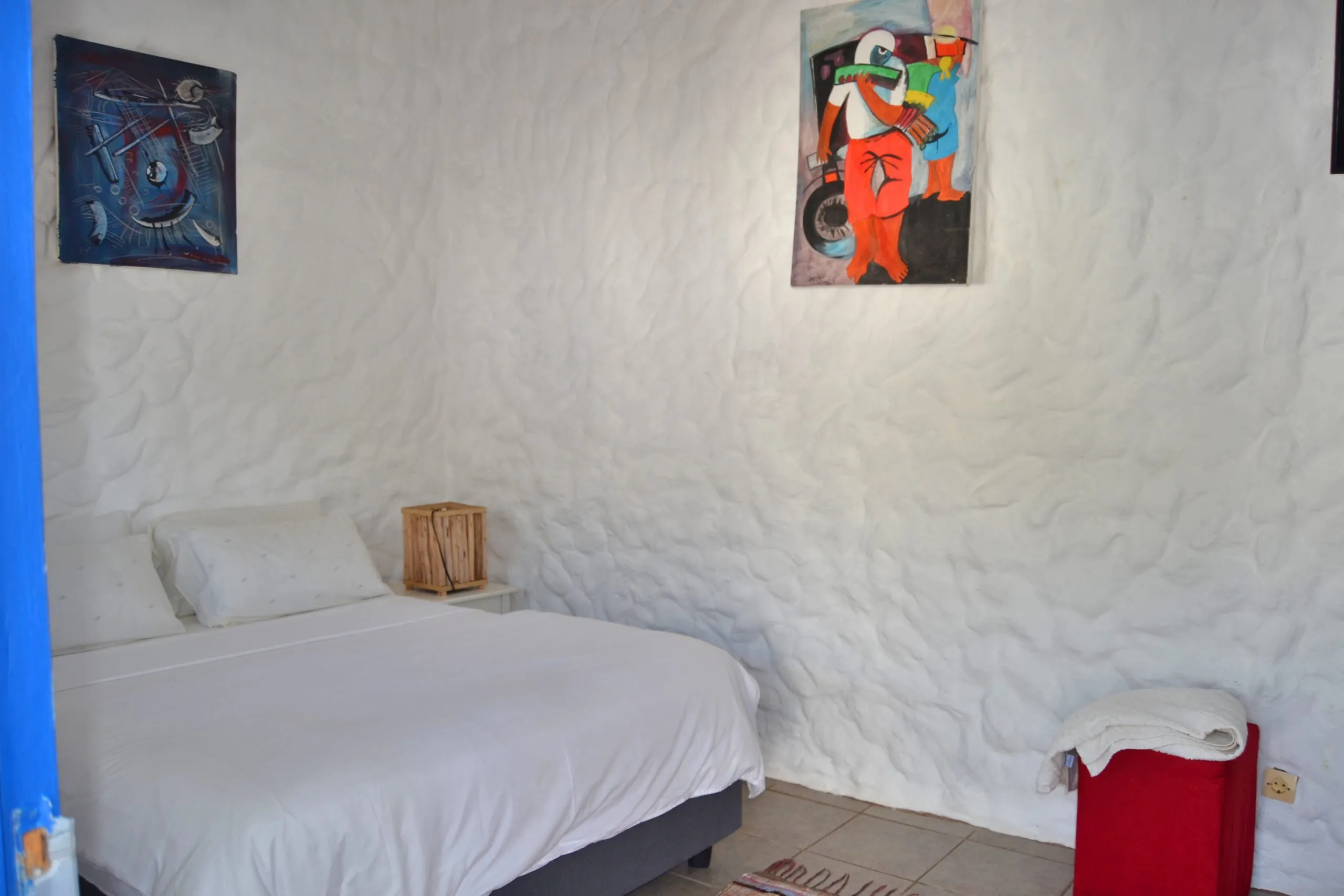 White bedroom with textured walls two paintings and a red laundry basket