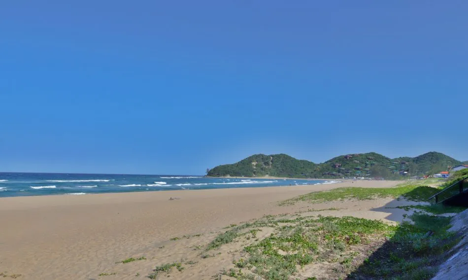 Sandy beach with green hills in the background under a clear blue sky