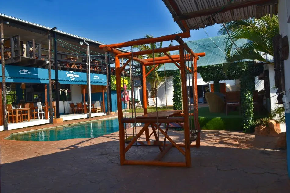 Swimming pool with wooden swing set in outdoor dining area under blue sky