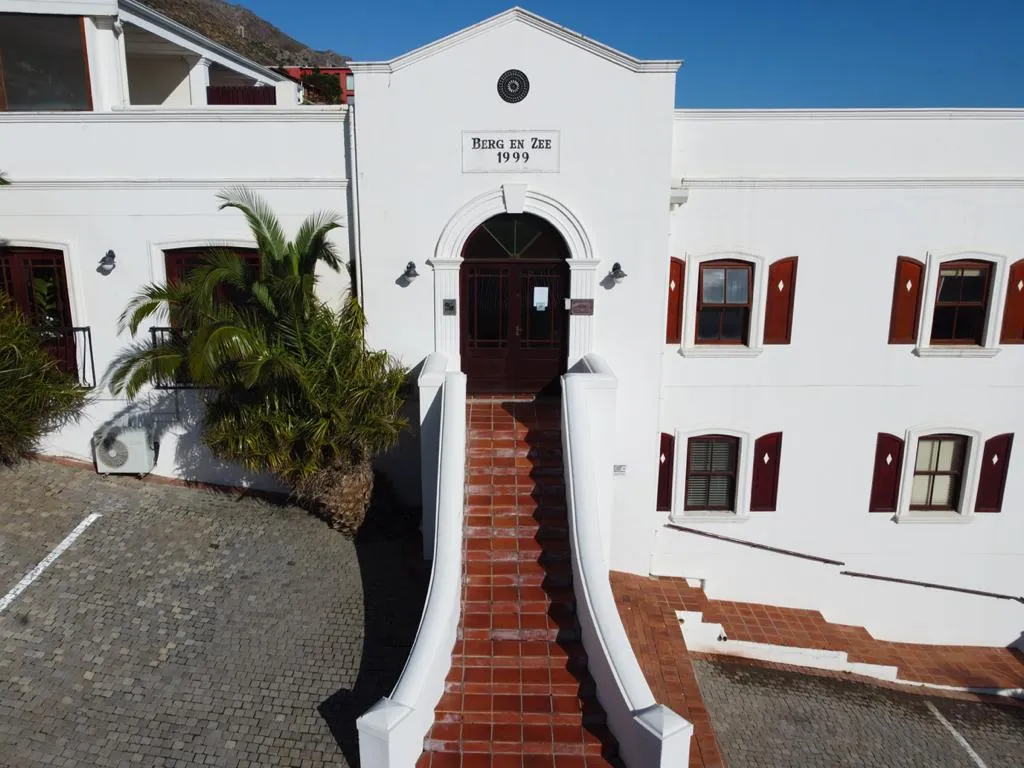 White building with redtiled steps leading to an arched entrance sunny day