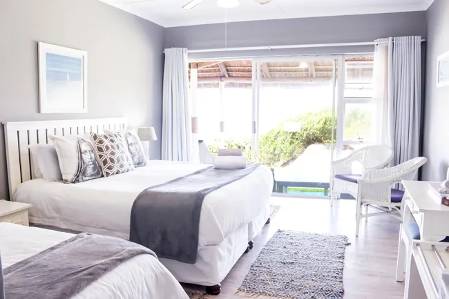 Bright bedroom with large bed sliding doors to garden and wicker chair