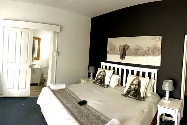 Bedroom with large bed pillows with faces and elephant painting on black wall