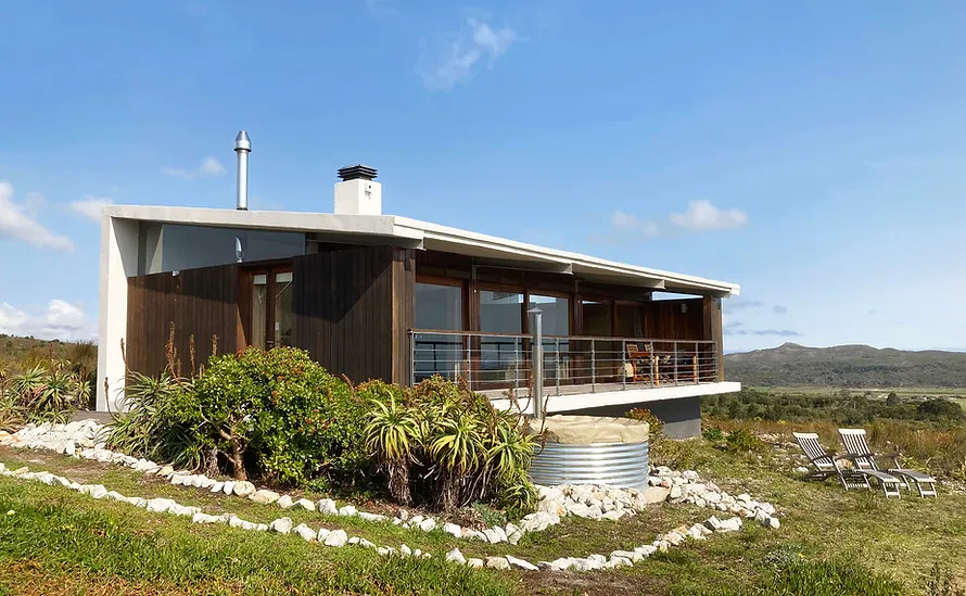 Modern house with large windows and deck surrounded by greenery and mountains in background