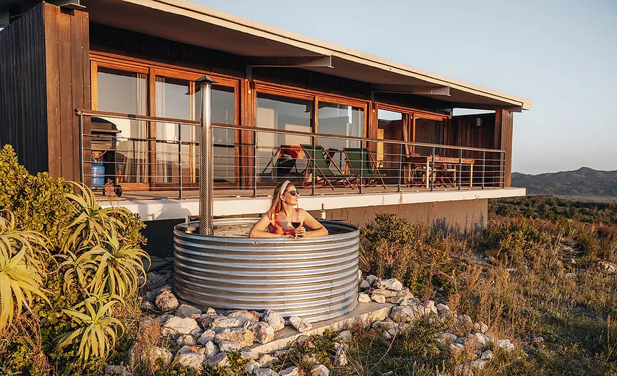 Woman relaxing in a metal hot tub outside a modern house with mountain views