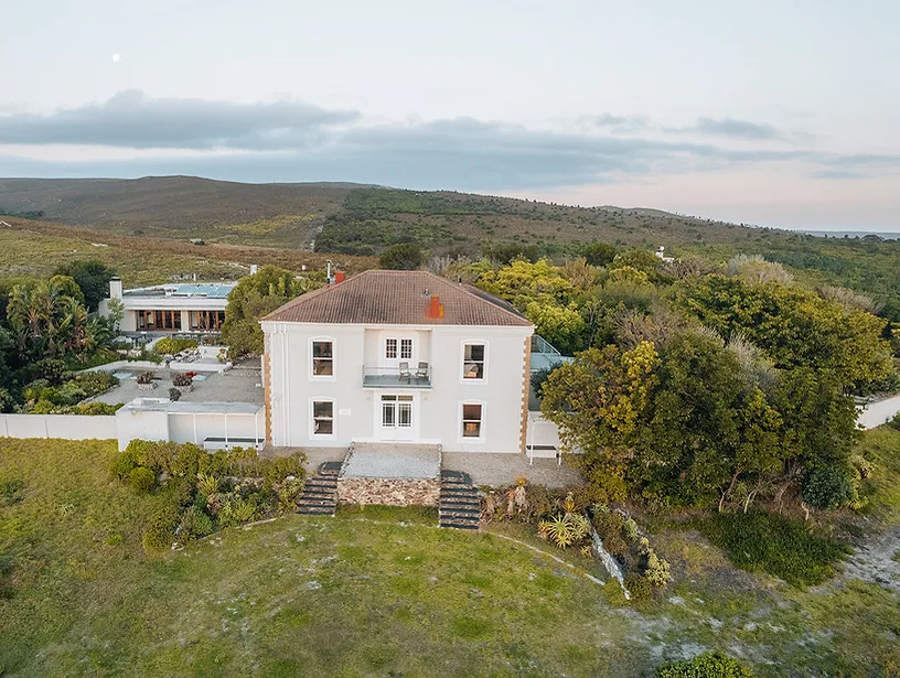 White house with red roof in a green hilly landscape at sunset
