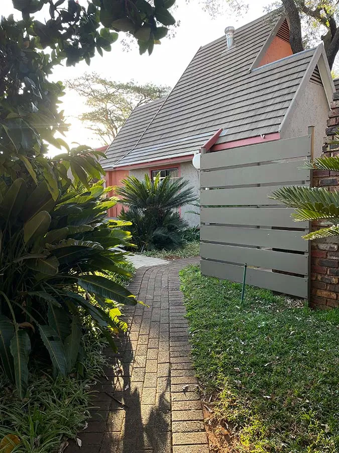 Pathway leading to a house with a sloped roof surrounded by greenery
