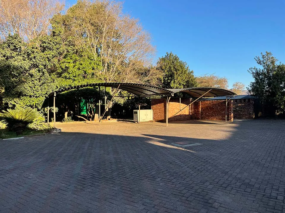 Outdoor paved area with curved metal roof structures and trees in the background