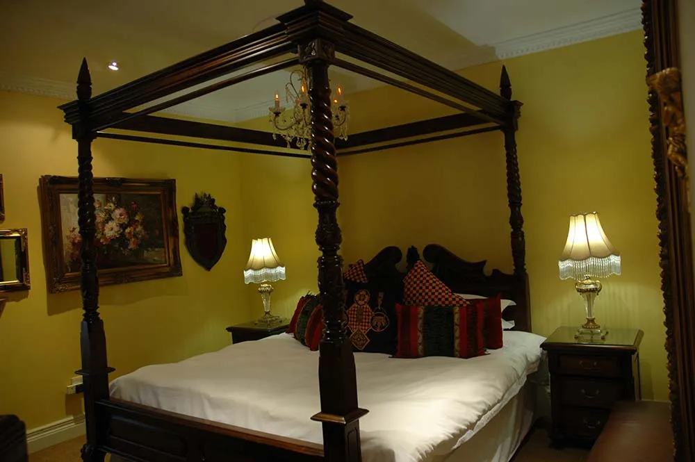 Fourposter bed with ornate headboard in a yellow bedroom with floral painting
