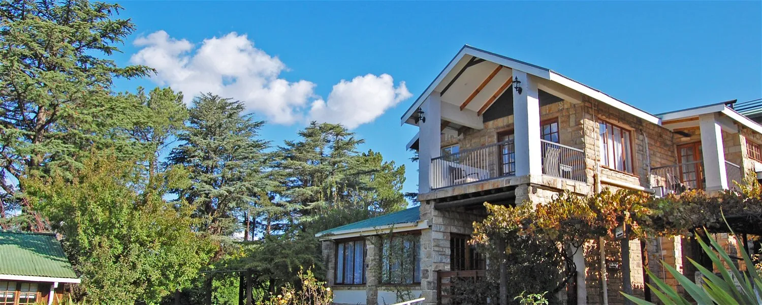 Twostory house with stone facade and wooden balcony surrounded by lush greenery