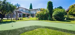 House with a putting green in the front yard surrounded by trees and shrubs