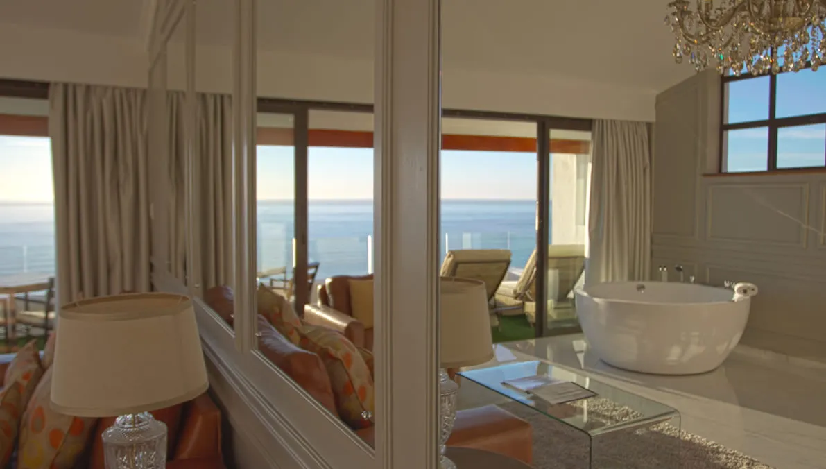 Modern bathroom with large mirror reflecting ocean view and luxurious seating area