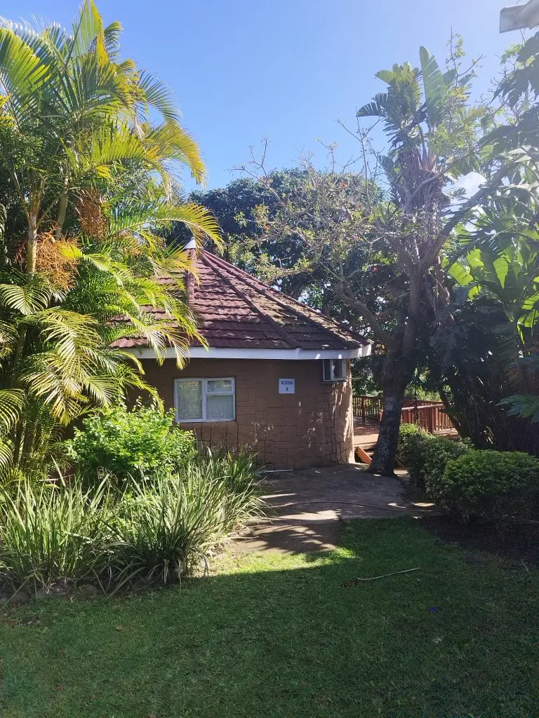 Small brick building with a red tiled roof surrounded by lush greenery