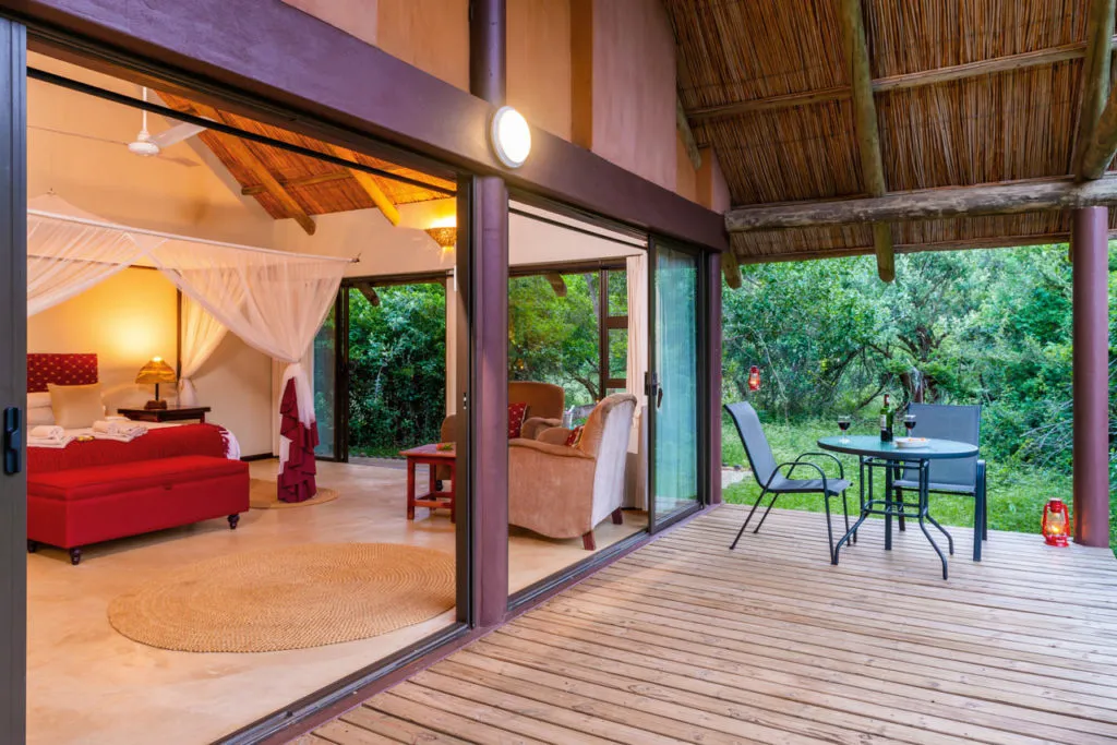 Wooden chalet with open doors to a deck overlooking a lush green forest