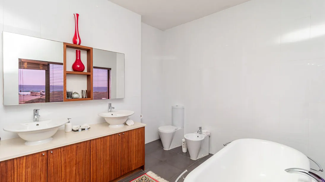 Modern bathroom with double sinks bathtub bidet and red vases on shelves