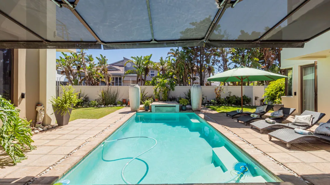 Swimming pool with lounge chairs and green umbrella in a backyard setting
