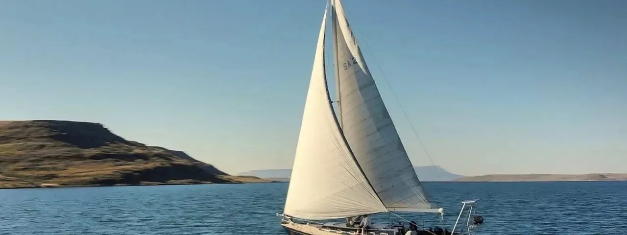 Sailboat with white sails on a calm sea with hills in the background