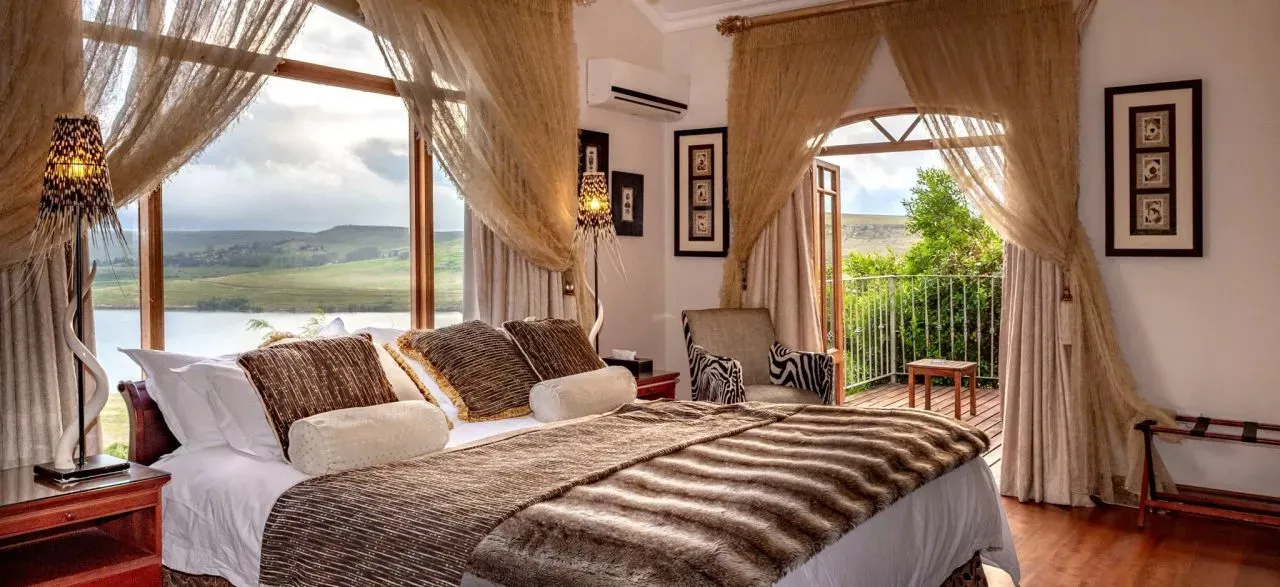 Bedroom with large windows overlooking a lake decorated with elegant curtains and bedding