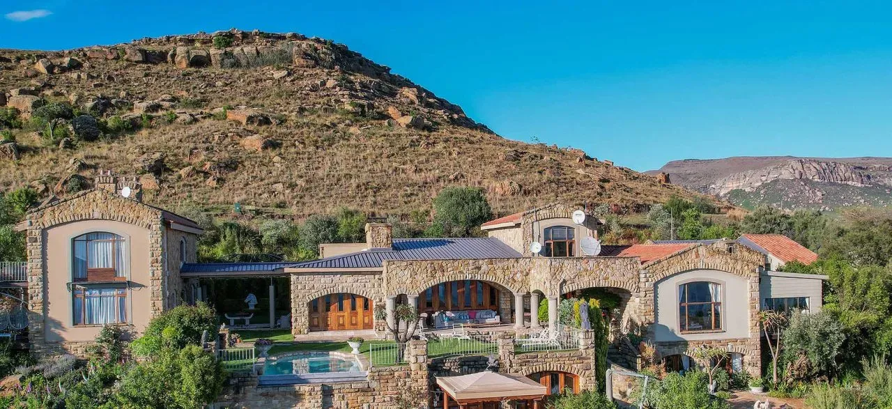 Large stone house with redtiled roofs in front of a mountainous landscape
