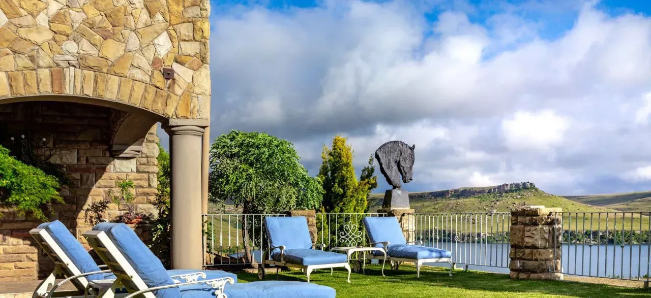 Stone patio with blue lounge chairs horse statue and lake view
