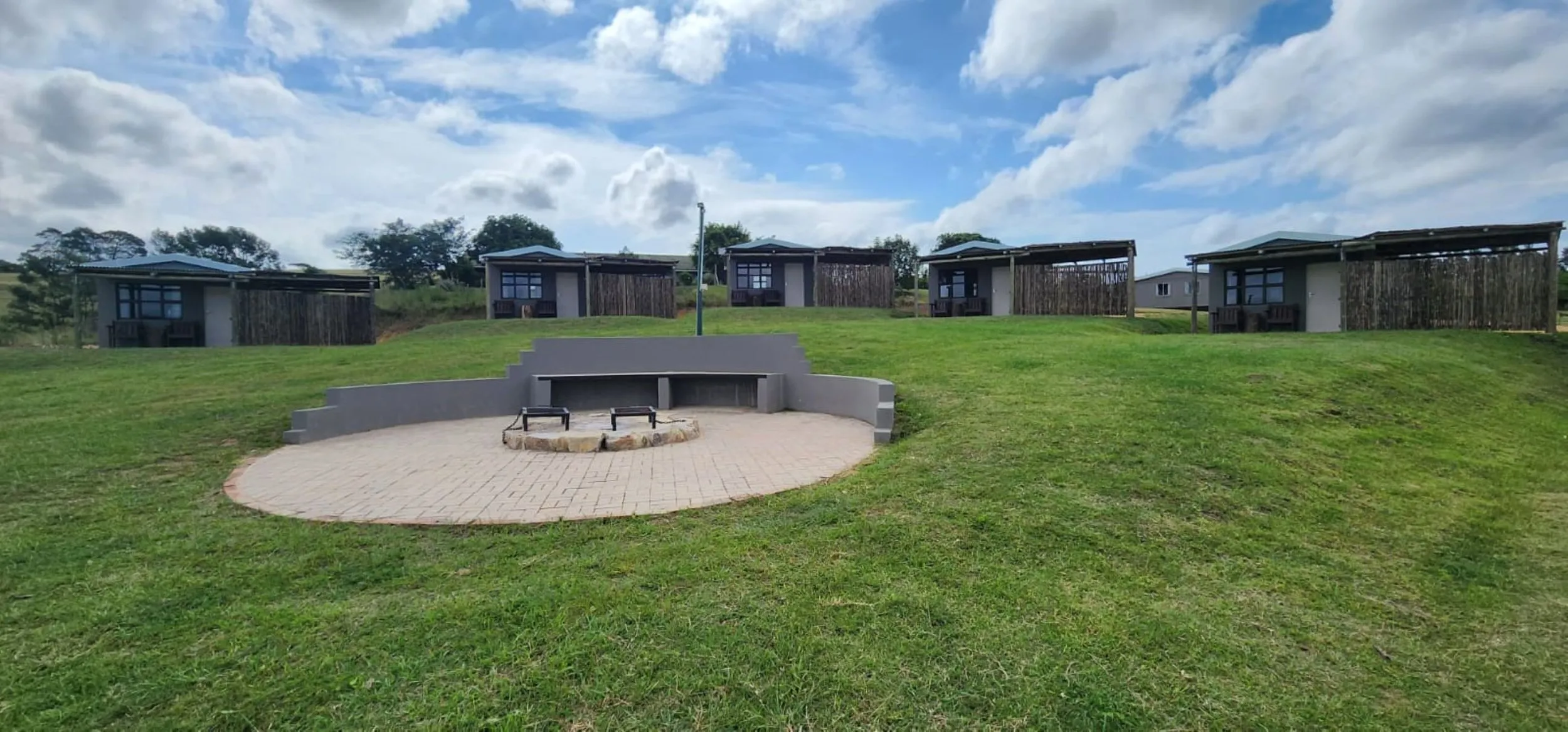 Row of modern cabins on a grassy hill with a circular stone seating area