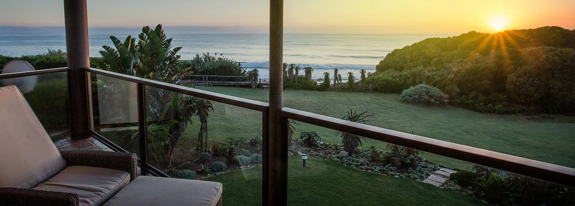 Sunset view from a balcony overlooking a grassy area and ocean
