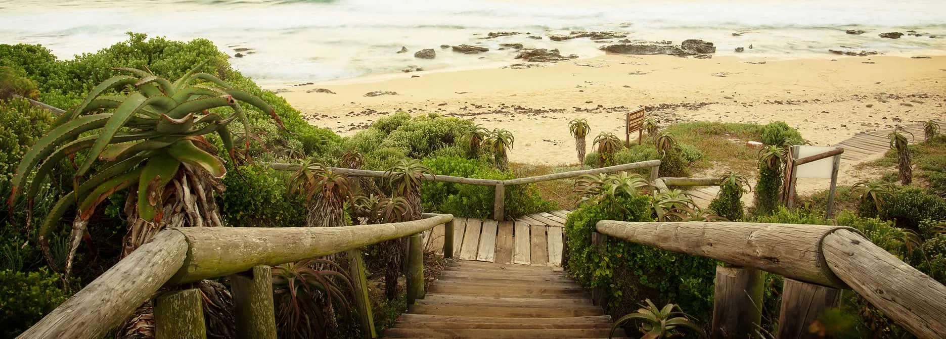 Wooden stairs leading to a sandy beach with ocean waves in the background