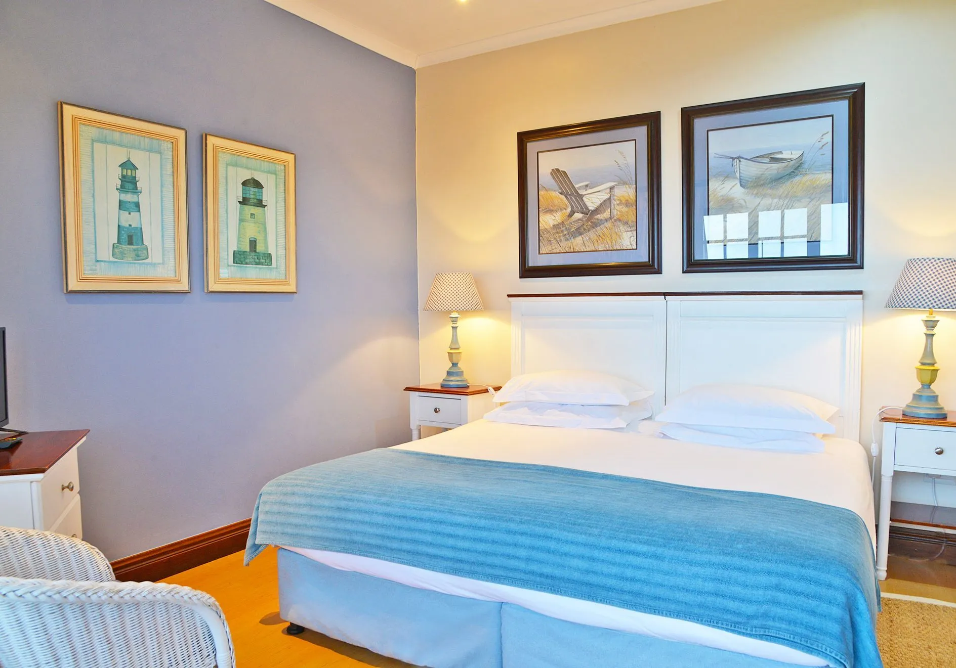 A neatly made bed in a bedroom with lighthousethemed artwork on the walls