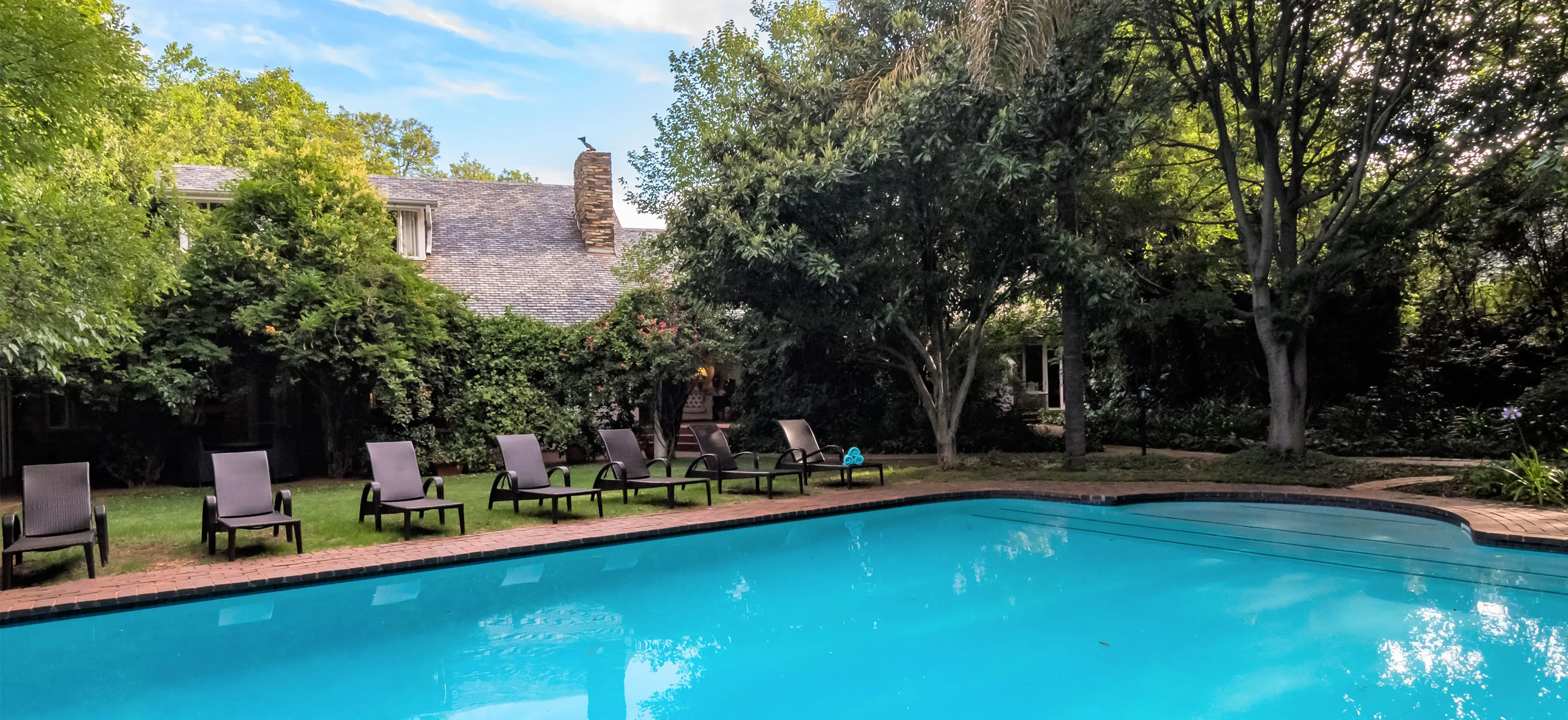 Swimming pool with lounge chairs surrounded by trees and a house in the background