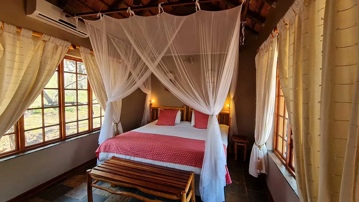 Bedroom with large bed canopy wooden bench and large windows with curtains